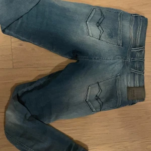 Blå jeansbyxor - Säljer ett par klassiska blå jeans i bra skick. De har en slim passform och är perfekta för vardagsbruk. Byxorna har en snygg tvätt och är utrustade med både dragkedja och knappar. Perfekta för höst och vår! Replay, model anbass. Strl 28/32. S