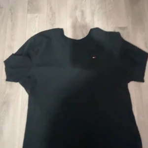 Svart t-shirt från Tommy Hilfiger - Säljer en klassisk svart t-shirt från Tommy Hilfiger. Den har en liten logga på bröstet och är i ett mjukt bomullsmaterial. Perfekt för vardagsbruk eller att styla upp med en snygg jacka. Passar till alla tillfällen!