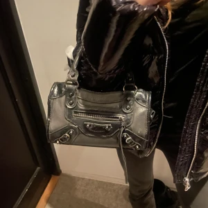 Svart axelväska med text - Säljer en cool och snygg svart axelväska i skinn med en unik rosa text på framsidan. 