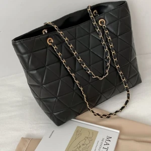 Svart axelväska - Snygg svart axelväska i quiltat mönster med kedjedetaljer på remmarna. Perfekt för både vardag och fest. Väskan har en stilren design och är rymlig nog för alla dina nödvändigheter.