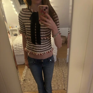 Fest topp - Säljer en superfin randig topp från Zara Woman i storlek XS. Den är i ett tjockare material med ränder i svart, vitt och rött. Toppen har korta ärmar och en söt svart rosett framtill. Perfekt för både vardag och fest! Jätte fin och unik!!