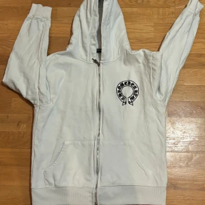 Vit hoodie från Chrome Hearts - Säljer en snygg vit hoodie från Chrome Hearts i storlek M . Den har en dragkedja framtill och en cool broderad logga på bröstet. Perfekt för höst och vår, och den är i mycket bra skick. Grym för både chill och festliga tillfällen! 🖤