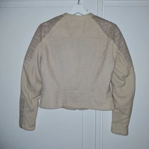 Beige jacka från H&M med fejk mocka detaljer  - Säljer en snygg beige jacka från H&M i mycket bra skick. Jackan har quiltade detaljer på axlar och ärmar, samt en dragkedja framtill. Perfekt för höst och vår med sin stilrena design och bekväma passform. Passar både till vardags och lite finare tillfällen.