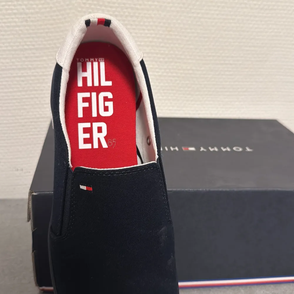 Snygga svarta sneakers från Tommy Hilfiger i helt nytt skick aldrig använt . De har en stilren design med vita detaljer och en röd sula. Perfekta för både vardag och fest. Skorna har en bekväm passform och är lätta att matcha med olika outfits.. Skor.