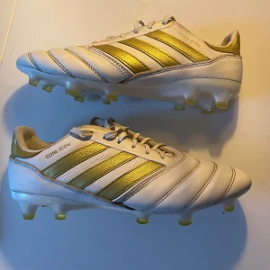 Adidas Copa Icon fotbollsskor - Säljer ett par Adidas Copa Icon fotbollsskor i vitt och guld. Skorna är i bra skick med klassisk snörning och en stilren design. Perfekta för fotbollsspelare som vill ha både stil och funktion på planen. Sulan har bra grepp för gräsplaner. Nypris (2699kr)