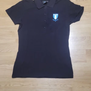 Svart pikétröja från Malmö FF - Säljer en svart pikétröja från Malmö FF. Den har en klassisk krage och knappar framtill. Perfekt för att visa ditt stöd för laget! Tröjan är i bra skick och passar både till vardags och matchdagar.