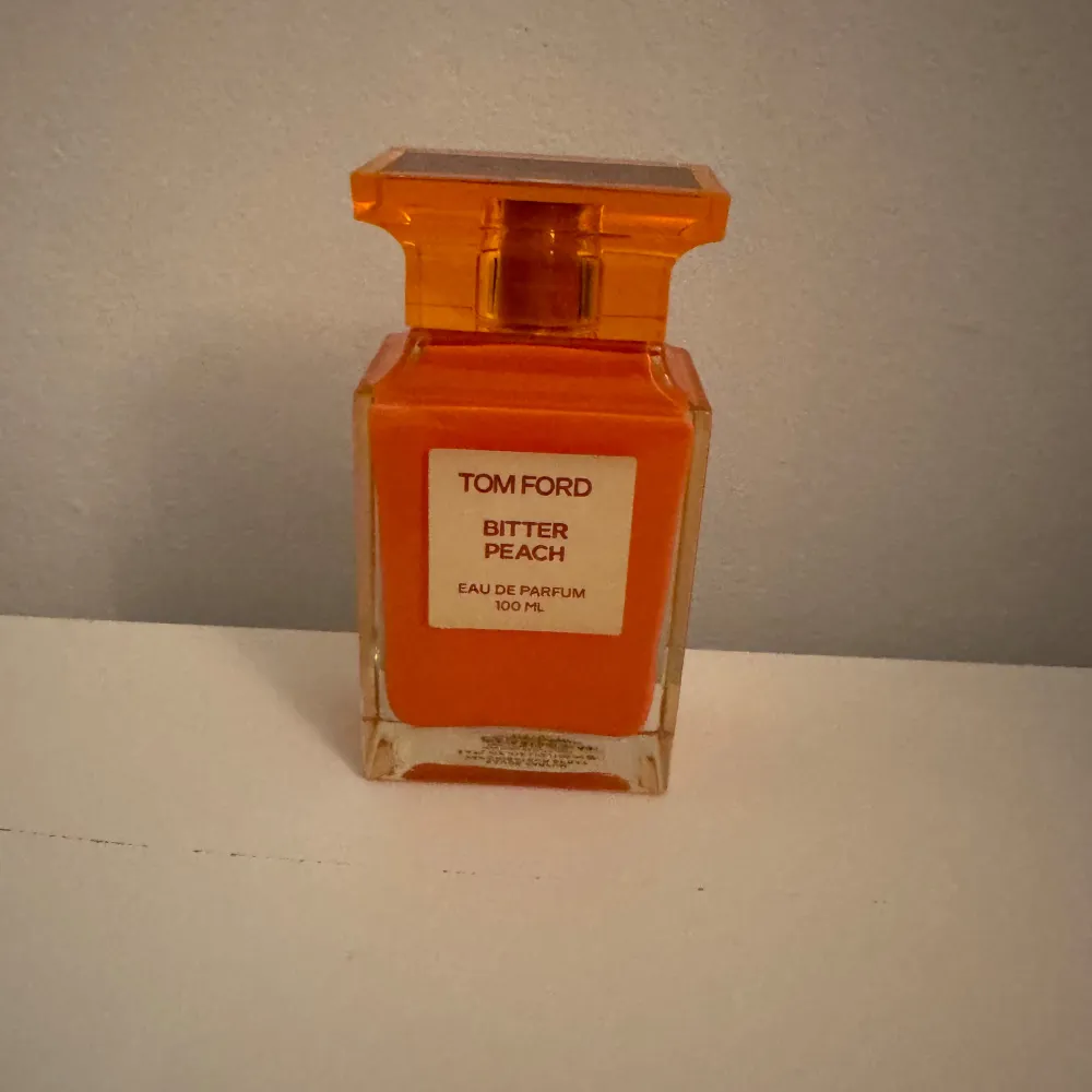 Säljer en lyxig Tom Ford Bitter Peach Eau de Parfum i en snygg orange flaska. Den rymmer 100 ml och har en fruktig och sensuell doft. Perfekt för dig som vill sticka ut med en unik och djärv parfym. Flaskan har en elegant design med en fyrkantig form och ett matchande lock.. Parfym.