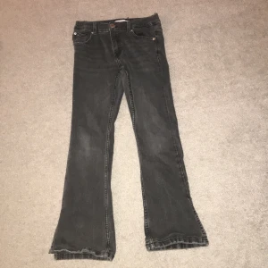 Grå jeansbyxor från Zara - Säljer ett par grå jeansbyxor från Zara i storlek 11-12 år. Byxorna har en bootcut-stil och är i bra skick. De har en klassisk femficksdesign och en knapp med Zara-logga. Perfekta för både vardag och fest!