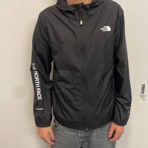 Svart vindjacka från The North Face - Säljer en svart vindjacka från The North Face i storlek L Barn. Jackan har en dragkedja framtill och är långärmad med logotypen tryckt på bröstet och ärmen. Perfekt för höst och vår, och den är i mycket bra skick. Passar både till vardags och lättare utomhusaktiviteter.