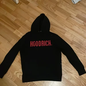Svart hoodie från Hoodrich - Säljer en svart hoodie från Hoodrich i bra skick. Den har en stor röd logga på framsidan och en klassisk känguruficka. Perfekt för höst och vinter, och den är superbekväm att ha på sig. Passar både till vardags och chillkvällar. Hör av dig om du är intresserad! Ny pris 800