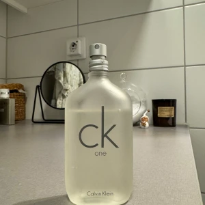 CK One parfym från Calvin Klein - Säljer en klassisk CK One parfym från Calvin Klein. Flaskan är genomskinlig med en stilren design och grå text. Perfekt för både vardag och fest! Flaskan är stor och innehåller mycket parfym, så den räcker länge. Passar både herr och dam. Innehåller ca 43ml