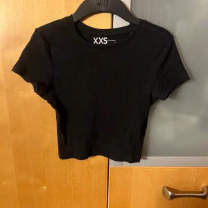 Svart ribbad croppad topp från H&M - Säljer en svart ribbad croppad topp från H&M i storlek XXS. Den är kortärmad och perfekt för sommardagar eller som ett lager under en jacka. Toppen är i mycket bra skick och har en tight passform. Perfekt för en casual look eller en utekväll! Köparen står för frakten🥰