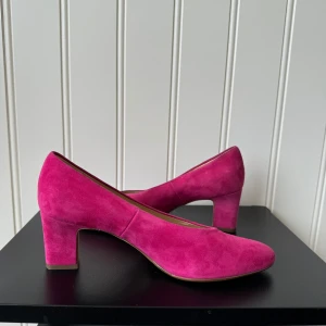 Rosa mockapumps från Peter Kaiser - Snygga rosa mockapumps från Peter Kaiser i storlek 36. De har en elegant klack och spetsig tå, perfekt för både fest och vardag. Skorna är i mycket bra skick och ger en färgklick till vilken outfit som helst.