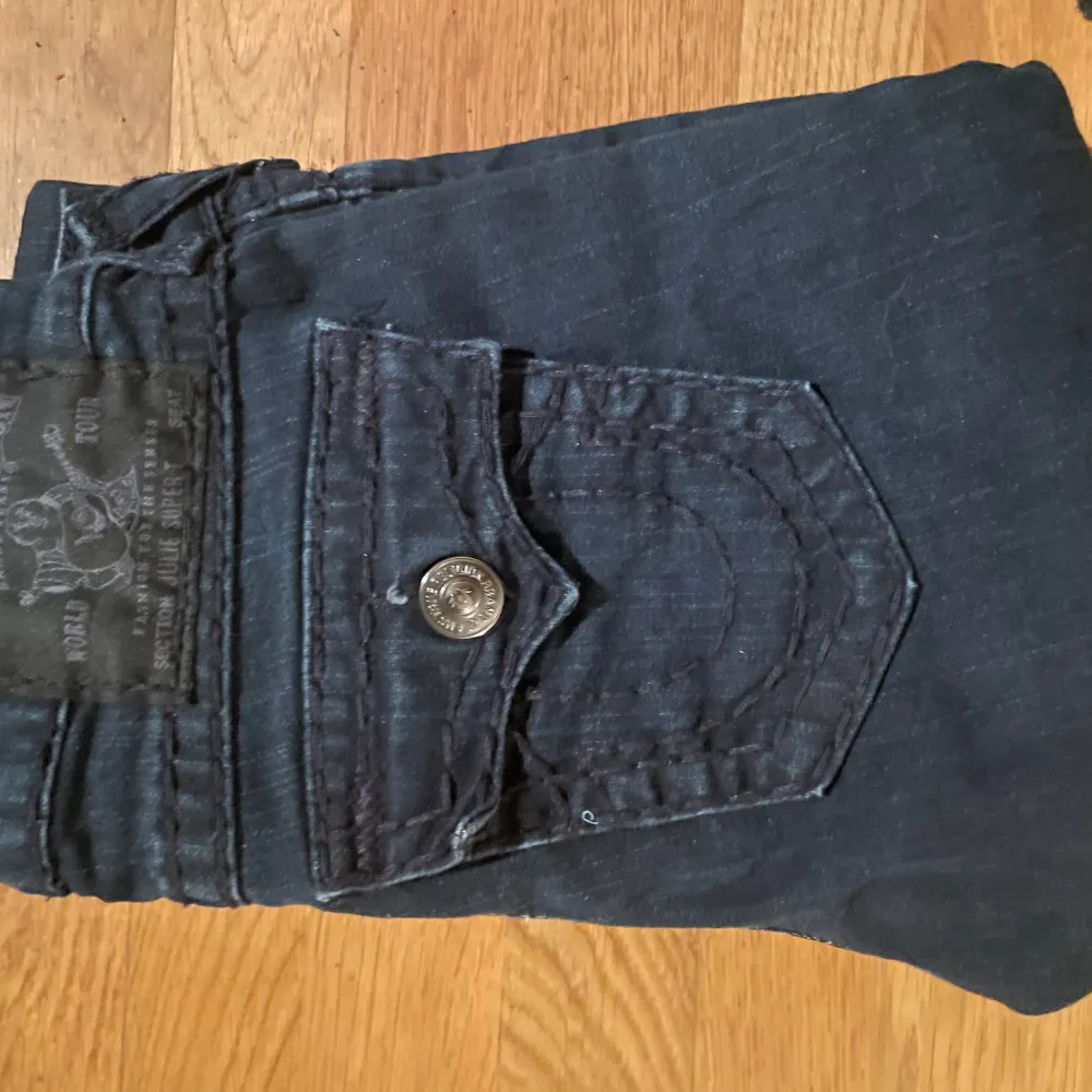 Säljer ett par snygga mörkblå jeans från True Religion. De har en tight passform och är i mycket bra skick. Jeansen har coola detaljer som knappar och fickor med lock baktill. Perfekta för både vardag och fest!. Jeans & Byxor.