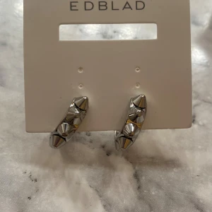 Silvriga örhängen från Edblad - Snygga och moderna silvriga örhängen från Edblad.🤩De har en cool design med små pyramidformade detaljer som ger en edgy look. Perfekta för att piffa upp vilken outfit som helst, oavsett om det är till vardags eller fest.🪩Kommer i originalförpackning. Helt oanvända. Säljer eftersom att jag råkade köpa två par. (Frakten betalas av köparen eller så kan vi mötas upp i Stockholm)