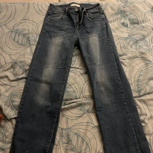 Blå jeans i bra skick (åt de lågmidjade hållet)  - Säljer ett par klassiska blå jeans i bra skick. De har en straight passform och är perfekta för vardagsbruk. Jeansen har en dragkedja och knapp framtill samt fem fickor. De är slitna på ett snyggt sätt för en cool look. Perfekta för både höst och vår!  Dom är även stretchiga 
