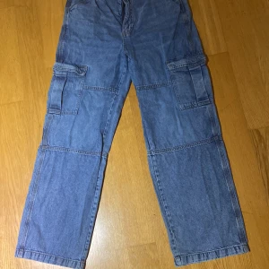 Blå cargopants  - Säljer ett par blå cargopants i jeansmaterial. De har flera praktiska fickor på sidorna och en loose passform som ger en avslappnad stil. Perfekta för vardagsbruk eller en casual utflykt. Byxorna är i bra skick och redo för nya äventyr! Jag säljer dom eftersom dom har blivit för stora för mig !😊