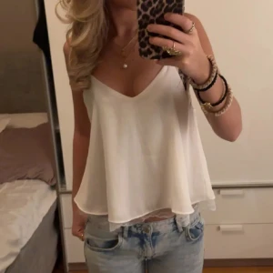 Vit ärmlös topp med spetsdetaljer - Säljer en superfin vit ärmlös topp med smala axelband och spetsdetaljer längst ner. Perfekt för sommardagar eller en utekväll. Toppen har en lös passform och är gjord i ett lätt och luftigt material.