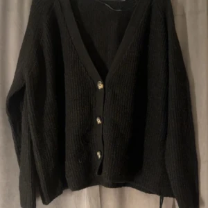 Svart stickad kofta - Mysig svart stickad kofta med knappar framtill. Perfekt för kyliga dagar och att mysa i hemma. Den har en enkel och stilren design som passar till det mesta. Ett måste i garderoben för höst och vinter!