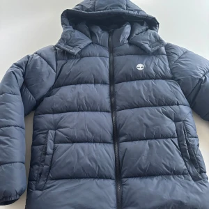Timberland jack Blå - Säljer en snygg blå pufferjacka från Timberland i storlek S. Jackan har en praktisk huva och dragkedja framtill. Perfekt för kalla dagar med sin varma och quiltade design. Den är i mycket bra skick och redo för nya äventyr! 💙