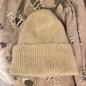 Beige stickad mössa - Mysig beige stickad mössa perfekt för kyliga dagar. Den har en ribbad design som ger extra värme och stil. Passar bra till både vardag och vinteraktiviteter. 