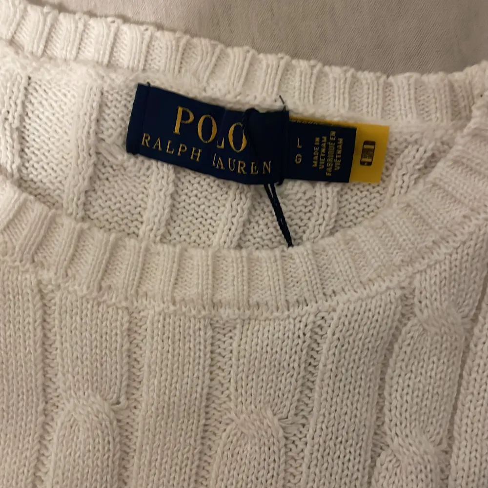 Säljer en snygg vit stickad tröja från Polo Ralph Lauren i storlek L. Tröjan har ett klassiskt kabelstickat mönster och den ikoniska loggan broderad på bröstet. Perfekt för både höst och vinter, och den är i nytt skick med etikett kvar. Supermysig och stilren!. Tröjor & Koftor.