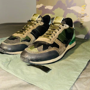 Valentino Rockrunner i camouflage - Säljer ett par snygga Valentino Rockrunner sneakers i camouflage. Skorna har en cool mix av gröna och svarta nyanser med läder- och mockadetaljer. De har en unik design med nitar på hälen och en bekväm sula. Perfekta för att ge din outfit en edgy touch! Skorna är perfekta till vintern som närmar sig. Storlek 41 passar 42 pris 1650 skick 8/10 kvitto finns!!