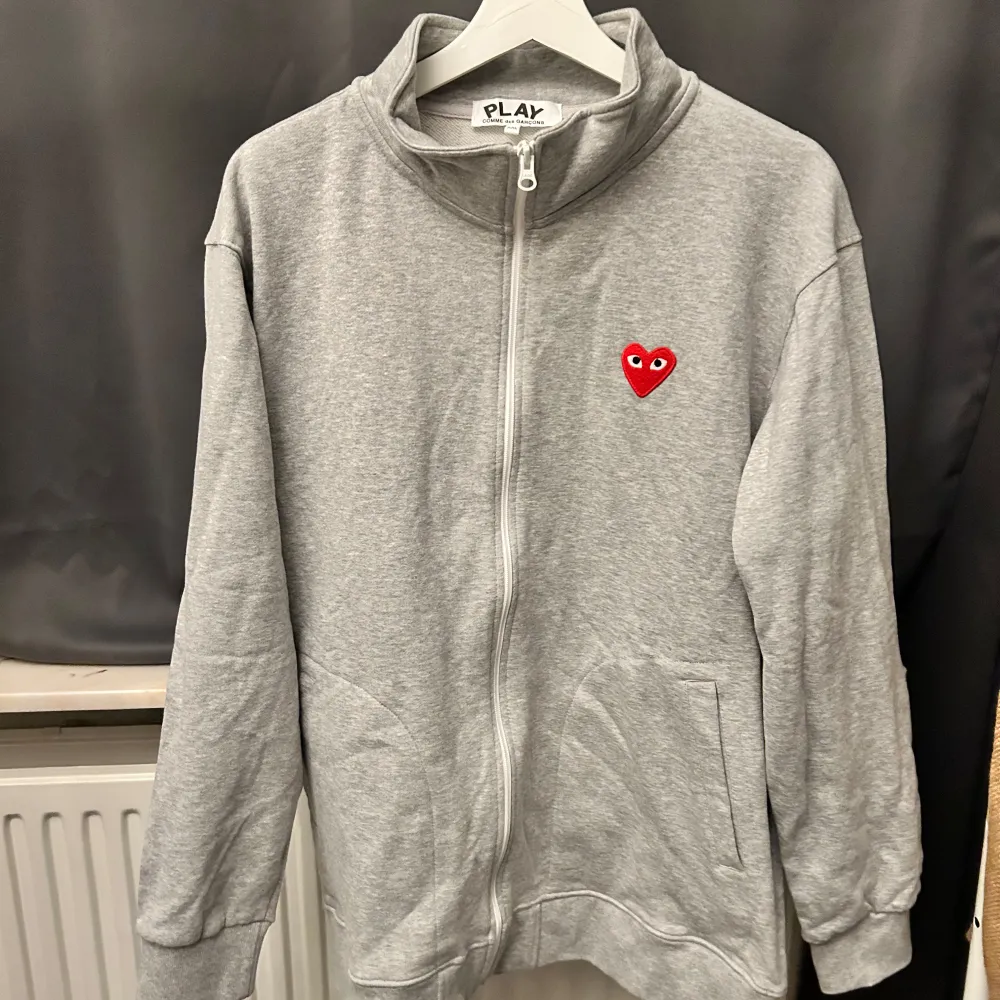 Säljer en grå hoodie från Comme des Garçons med det ikoniska röda hjärtmotivet på bröstet och flera på ryggen. Tröjan har dragkedja och är i mycket bra skick. Perfekt för höst och vår, och den är superbekväm att ha på sig. Passar både till vardags och lite mer avslappnade tillfällen. CDG har små storlekar så lappen säger XXL men den skulle passa XL också. Tröjor & Koftor.