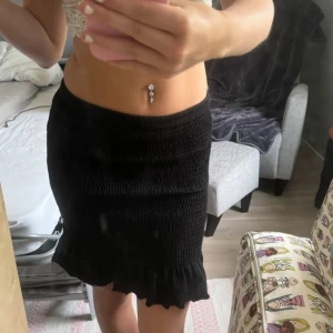 Svart kjol med volang - Säljer en superfin svart kjol med volangdetalj längst ner. Den är tight och perfekt för både vardag och fest. Kjolen är i ett stretchigt material som formar sig snyggt efter kroppen.