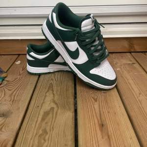 Säljer ett par snygga Nike Dunk sneakers i grönt och vitt. De har en klassisk design med snörning och är i mycket bra skick. Box tillkommer! 899kr pris! 