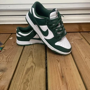 Nike Dunk i grönt och vitt - Säljer ett par snygga Nike Dunk sneakers i grönt och vitt. De har en klassisk design med snörning och är i mycket bra skick. Box tillkommer! 899kr pris! 