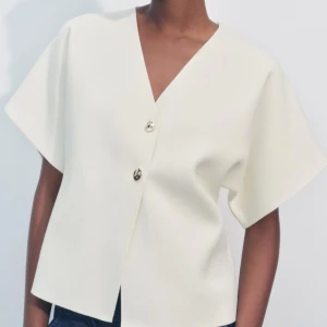 Vit kortärmad blus med knappar - Säljer denna super snygga vita blusen från Zara med korta ärmar och två stilrena knappar framtill. Perfekt för både vardag och fest. Den har en enkel och elegant design som passar till det mesta. Blusen är i ett lite tjockare mjukt material, slutesåld på hemsidan. Storlek M men passar även mig som brukar ha S-M, endast testad.