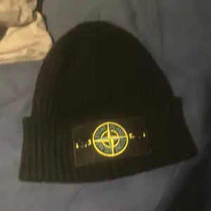 Säljer en snygg svart ribbad mössa från Stone Island. Den är tillverkad i Italien och har en cool broderad logga framtill. Perfekt för att hålla sig varm och stilren under kyliga dagar. Passar både till vardags och mer uppklädda tillfällen.