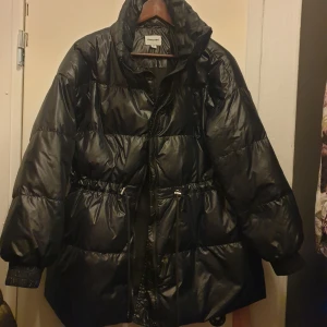 Svart pufferjacka - Säljer en svart pufferjacka/kappa Jackan har en glansig yta och är utrustad med dragkedja och justerbar midja. Storlek M. Kan inte se några defekter. Jackan är nytvättad.