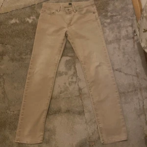 Beige byxor från Hugo Boss - Snygga beige byxor från Hugo Boss med klassisk design. Byxorna har en rak passform och är tillverkade i ett mjukt material. Perfekta för en stilren look.