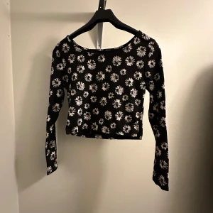 Svart blommig croppad topp - Snygg svart croppad topp med vita blommor. Toppen har långa ärmar och en rund halsringning. Från H&M. Hittar inte storleken men passar som M!