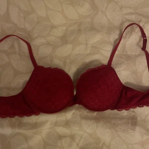 Röd spets-bh från Intimissimi - Säljer en röd bh från Intimissimi med spetsdetaljer. Den har justerbara axelband och en klassisk knäppning bak. Modellen är ”super push-up” så ganska mycket push och vaddering. Endast använd en gång💖Säljer då jag inte riktigt gillar modellen!