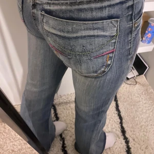 Blå jeans med broderade detaljer - Snygga blå jeans med broderade detaljer på bakfickorna. De har en lågmidjad passform och en bootcut-stil som ger en avslappnad look. Perfekta för en casual outfit.byxorna har en större bootcut än de flesta andra bootcut jeansen men är fortfarande super snygga. Skriv till mig vid minsta lilla💕