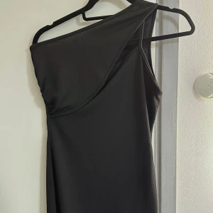 Svart oneshoulder cut out klänning - Tight svart klänning från Pretty Little Thing. Helt oanvänd. Passar bättre på personer med större byst! Kontakta mig gärna vid fler frågor om passform🫶🏼