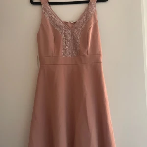 Rosa klänning från Bodyflirt - Elegant rosa klänning från Bodyflirt med spetsdetaljer vid halsringningen. Klänningen har en v-ringad design och breda axelband. Perfekt för en stilfull look.