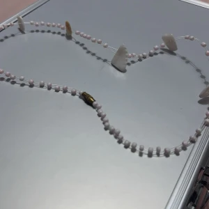 Ljusrosa  pärlhalsband Barn  - Elegant halsband med ljusrosa pärlor och unika vita sneckor. Har en guldfärgad låsdetalj som ger en lyxig touch. Perfekt för att lyfta vilken outfit som helst.