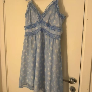 Blommig blå klänning från Vero Moda - Charmig blå klänning från Vero Moda med ett blommigt mönster. Klänningen har volangdetaljer och smala axelband. Perfekt för en somrig look.