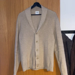 Beige kofta från John Henric - Säljer en stilren beige kofta från John Henric. Koftan har en klassisk design med knappar framtill och en mjuk krage. Perfekt för att hålla sig varm och snygg under kyligare dagar. Den är i väldigt bra skick. Pris kan diskuteras vid snabb affär.