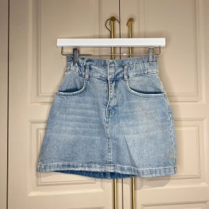 Jeanskjol i ljusblå denim - Trendig jeanskjol i ljusblå denim med hög midja och bälteshällor. Kjolen har en klassisk femficksdesign och en dragkedja framtill. Perfekt för en avslappnad stil.