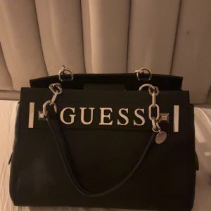 Svart handväska från Guess - Jag säljer min svarta väska från Guess! Den är äkta och ser helt ny ut och har bra med utrymme inne. Om ni är intresserade och vill ha mer information eller bilder på väskan skriv!🩵