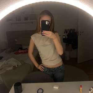 Beige ärmlös topp - Snygg beige ärmlös topp med en stilren design. Perfekt för en avslappnad look. Toppen har en lätt rynkad detalj på sidan som ger en fin passform.