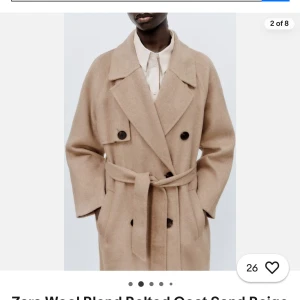 Beige kappa med bälte från Zara Ullmix strl S - Elegant beige kappa från Zara i ullblandning. Den har en klassisk dubbelknäppt design med stora svarta knappar och ett matchande bälte i midjan. Perfekt för kyligare dagar med sin långa passform och stilrena look. Oanvänd. Slutsåld mycket eftertraktad modell