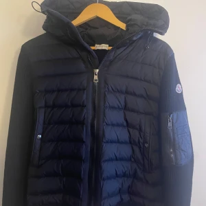 Moncler Cardigan - Snygg svart Cardigan från Moncler med huva och dragkedja. Jackan har ett quiltat mönster och är perfekt för kyligare dagar. Den har en praktisk ficka med dragkedja på ärmen och Moncler-logga på sidan. Väldigt bra skick. Kan finnas lite defekter från användning men ingen som syns så tydligt. Den är äkta men tyvär borttappat kvitto. Skriv om du har frågor eller önskar mer bilder. Priset går att förhandla vid snabb affär. Hoppas vi hörs 