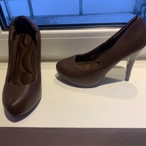 Bruna pumps med klack - Eleganta bruna pumps med hög klack och rundad tå. Perfekta för en stilren look.