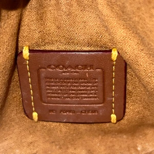 Vit axelväska från Coach - Snygg vit axelväska från Coach i skinn med dragkedja och gulddetaljer. Perfekt för att bära dina nödvändigheter med stil. Väskan har en elegant och kompakt design.